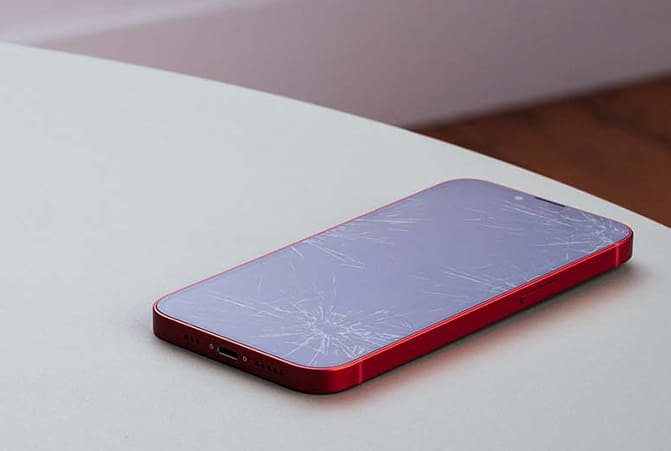 Een mobiele telefoon met een geroken display ligt op tafel.