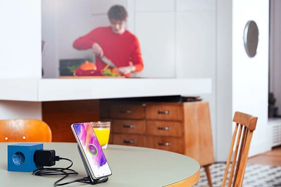 Een tiener kookt op de achtergrond, terwijl op de tafel een Samsung-smartphone in eeninductielader oplaadt.