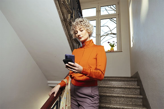 Een vrouw loopt een trap af en haar mobiele telefoon wordt via een powerbank opgeladen.