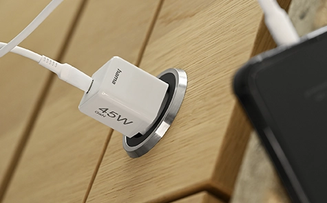 Een oplader van 45 watt wordt aangesloten op een stopcontact in een houten muur en laadt een smartphone op.