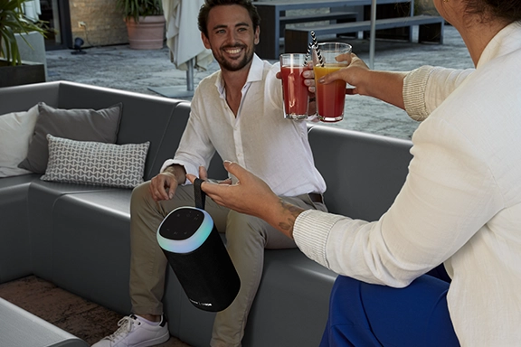 Twee vrienden zitten 's avonds ontspannen bij elkaar en luisteren naar muziek via de Hama Bluetooth®-luidspreker "Glow Pro".